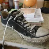 Une chaussure Converse noire usée, avec la semelle qui se décolle, témoigne de nombreuses aventures.