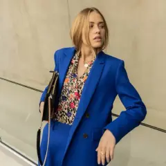 Une femme porte un tailleur-pantalon bleu vif avec une chemise à motifs colorés. Une belle idée tenue travail femme pour un look audacieux.