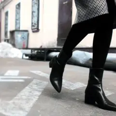 Une femme porte une tenue élégante avec des chelsea boots femme noires, un manteau à carreaux et des collants.
