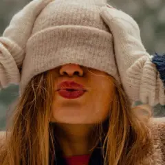 Une jeune femme s'amuse à s'habiller chaudement pour affronter le froid, cachant son visage sous un bonnet et des moufles.