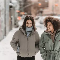 Deux amies profitent d'une promenade hivernale, bien emmitouflées dans leur vêtement contre le froid. Le top 7 des tenues chaudes pour affronter la neige.