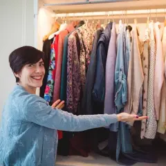 Une femme souriante devant une penderie remplie de vêtements colorés. Elle semble hésiter, car je n'arrive pas à jeter mes vêtements.
