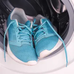 Paire de baskets bleues dans le tambour d'une machine à laver. Prêtes pour un cycle de nettoyage.