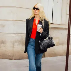 Femme blonde portant un jean évasé et un blazer rayé, avec un haut rouge vif et un sac à main noir.