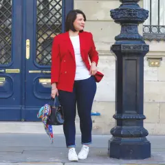 Une femme élégante montre comment porter un blazer rouge femme avec un jean et des baskets. Elle tient un sac noir orné d'un foulard coloré.