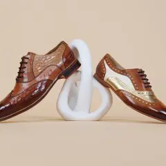 Comment porter des richelieu femme : deux paires de chaussures élégantes en cuir marron, ornées de textures et de détails dorés, posées sur un socle blanc.