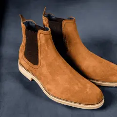 Paire de bottines Chelsea en daim marron, sur fond bleu nuit. La matière daim offre une texture douce et luxueuse.