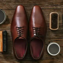 Paire de chaussures en cuir marron, prête pour un entretien. Brosse, cirage et chiffon pour protéger le cuir de la pluie.