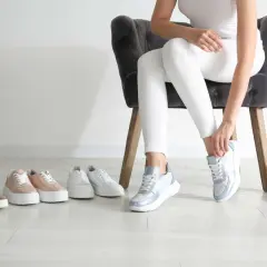 Choix de baskets pour une petite taille : une femme essaie des baskets bleues et blanches, entourée de plusieurs paires de chaussures.
