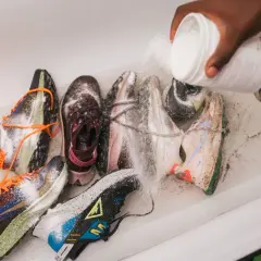 Une main verse une poudre blanche sur plusieurs paires de baskets dans une baignoire. C'est une étape clé pour savoir comment désinfecter des chaussures.