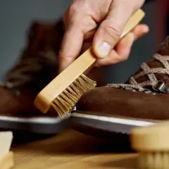 Maintenir vos chaussures en daim beige impeccables : une main utilise une brosse pour nettoyer le daim.