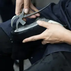 Un artisan utilise un outil pour travailler sur un objet en simili cuir noir. La question "peut on peindre du simili cuir" se pose face à cette métamorphose.