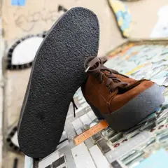 Une semelle crêpe noire repose contre une chaussure marron en daim. Le motif texturé de la semelle crêpe offre une adhérence robuste.