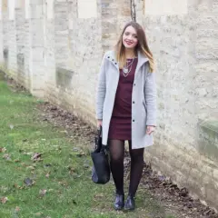 Une femme porte une robe bordeaux et un manteau gris clair. L'association couleur bordeaux vêtements est élégante.