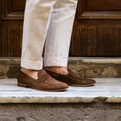 Pieds chaussés de mocassins marron en daim, un look estival parfait pour des chaussures sans chaussettes.