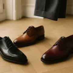Trois paires de chaussures habillées, dont une chaussure marron, prêtes à accompagner un costume gris.
