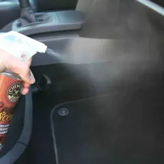 Une main vaporise un produit pour voiture, diffusant une agréable odeur de cuir dans l'habitacle.