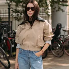 Une femme avec une morphologie H porte un jean bleu délavé et une veste beige.