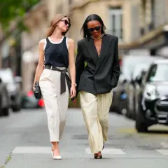 Deux femmes marchent dans la rue. L'une porte un pantalon blanc et un top noir, l'autre un blazer noir et un pantalon rayé. Idées pour comment s'habiller quand on est mince et petite.
