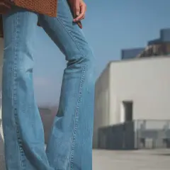 Un jean bootcut bleu clair, un pull marron et des baskets. Style décontracté pour une journée ensoleillée.