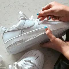 Main blanche, on nettoie une chaussure qui couine avec un coton-tige. Les ongles sont décorés de visages souriants.