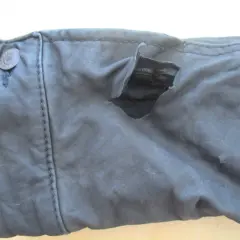 Gros accroc sur un vêtement en cuir, révélant la doublure intérieure. Le bouton sur le côté gauche est intact.