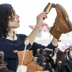 Une femme aux cheveux bouclés brosse une botte en cuir. Elle s'assure de la bonne fréquence de cirage de ses chaussures pour les garder en parfait état.