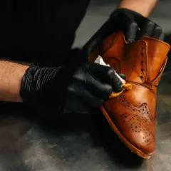 Gants noirs pour un entretien simili cuir. Un homme nettoie une chaussure marron avec un chiffon.
