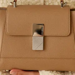 Sac à main élégant en cuir grainé camel, orné d'un fermoir métallique texturé.