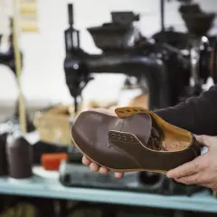 Un artisan examine une chaussure de ville en cuir marron, signe qu'il est temps de penser à quand changer ses chaussures de ville.