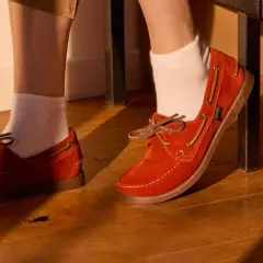 Chaussure bateau femme look : des mocassins en daim orange vif avec lacets en cuir, portés avec des chaussettes blanches sur un parquet en bois.