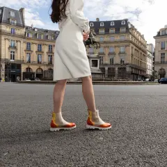 Une femme porte des bottines colorées en plein été, marchant sur une place parisienne.