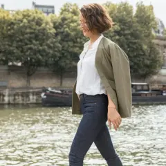 Une femme élégante à Paris, parfaite pour savoir comment s'habiller quand il fait 10 degrés femme : jean, chemise blanche et veste kaki.
