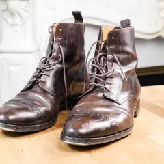 Paire de bottines en cuir griffé marron foncé, lacets serrés, posées sur une table en bois.