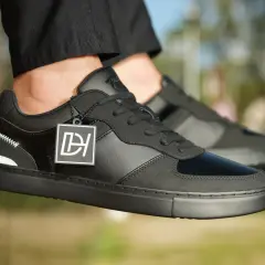 Baskets noires stylées, avec un jean qui détient sur la chaussure. Logo DH sur une étiquette.