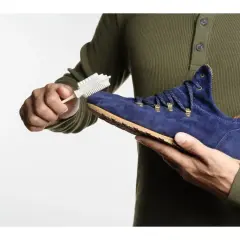 Maintenir le cuir suédé en bon état : une main brosse une chaussure bleue avec une brosse spéciale.