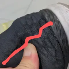 Un pouce appuie sur le contrefort d'une chaussure noire, révélant une fissure.