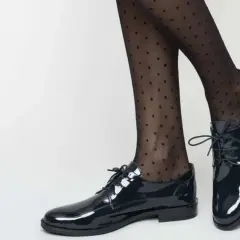Pieds chaussés de derbies vernies et collants à pois. Idéal pour savoir comment porter des derbies femme avec élégance.