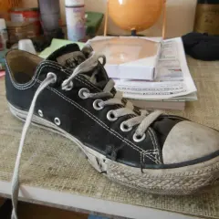 Une chaussure Converse noire usée, avec la semelle qui se décolle, témoigne de nombreuses aventures.