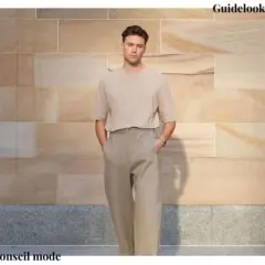 Un homme grand et mince porte un t-shirt beige et un pantalon ample. Un look parfait pour savoir comment s'habiller quand on est grande et mince.
