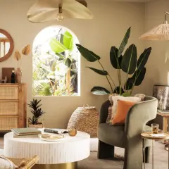 Salon bohème avec meubles en rotin et touches dorées. Le vert du fauteuil et l'orange du coussin s'accordent bien avec le doré.