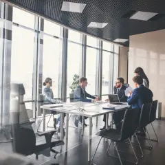Des employés en tenue pour réunion travail discutent autour d'une table dans une salle de conférence lumineuse avec vue sur la ville.
