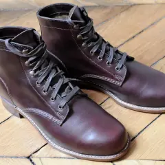 Bottes marron en cuir gras, lacets gris, sur un parquet en bois.