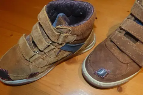 Paire de bottines marron avec des patchs noirs et roses sur le bout de chaussure abîmé.