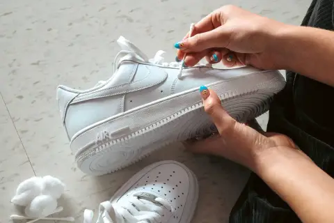 Main blanche, on nettoie une chaussure qui couine avec un coton-tige. Les ongles sont décorés de visages souriants.