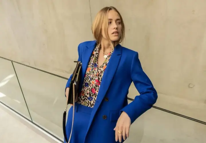 Une femme porte un tailleur-pantalon bleu vif avec une chemise à motifs colorés. Une belle idée tenue travail femme pour un look audacieux.