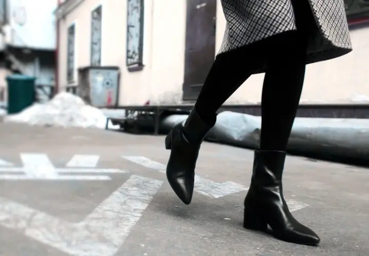 Une femme porte une tenue élégante avec des chelsea boots femme noires, un manteau à carreaux et des collants.