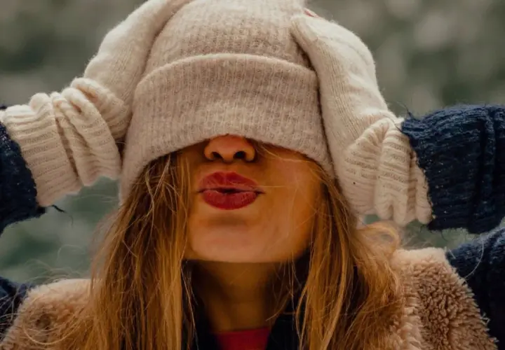 Une jeune femme s'amuse à s'habiller chaudement pour affronter le froid, cachant son visage sous un bonnet et des moufles.
