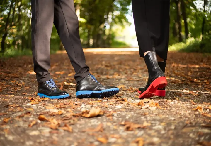 Deux paires de chaussures sur un sentier automnal. L'une a une semelle gomme ou caoutchouc bleue vive, l'autre une semelle rouge éclatante.