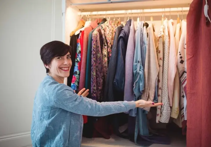 Une femme souriante devant une penderie remplie de vêtements colorés. Elle semble hésiter, car je n'arrive pas à jeter mes vêtements.